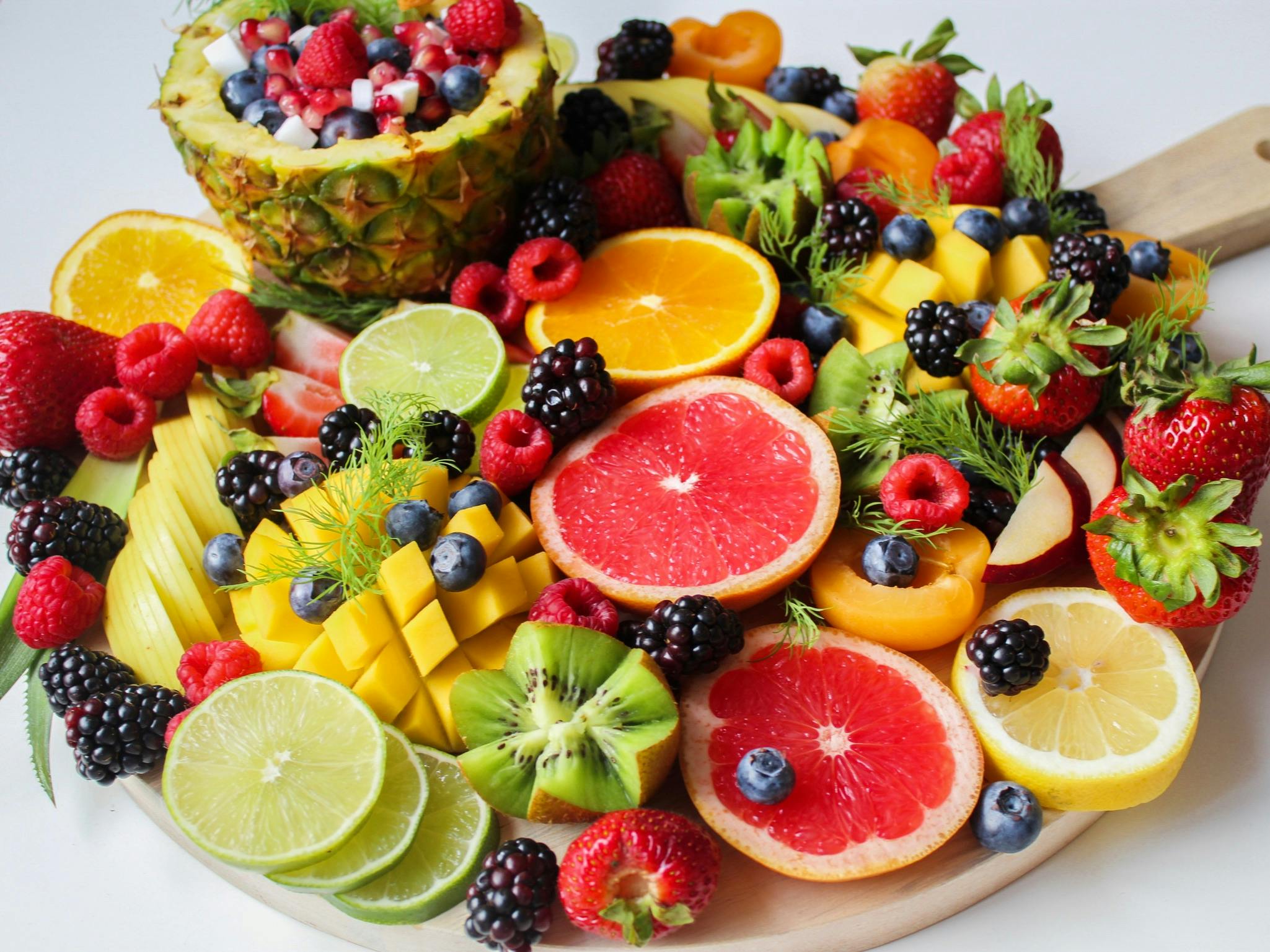 A tray filled with a colorful assortment of sliced fruits, including mango, kiwi, and strawberries, arranged neatly for serving.
